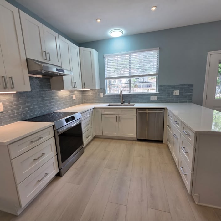 Remodeled kitchen with white cabinets, blue-green tile backsplash, pale countertops, and light wood-look flooring.