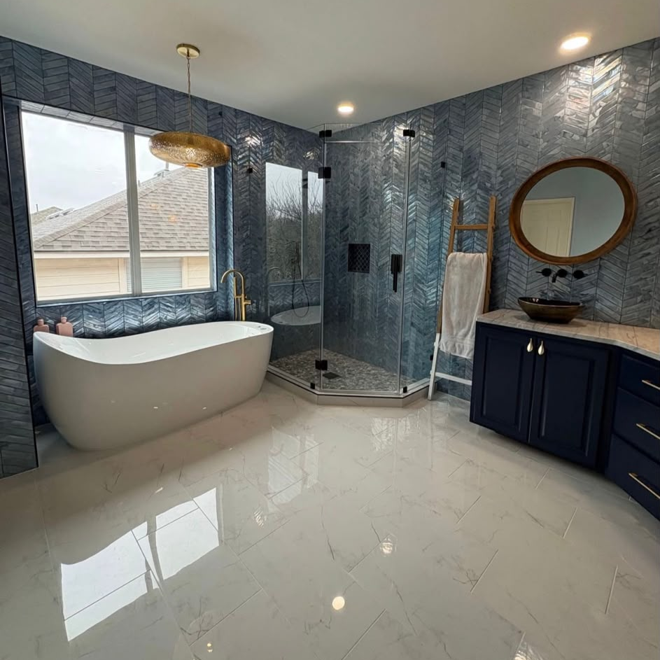 Remodeled master bathroom with a freestanding white tub, glass corner shower, blue patterned wall tile, and navy vanity.