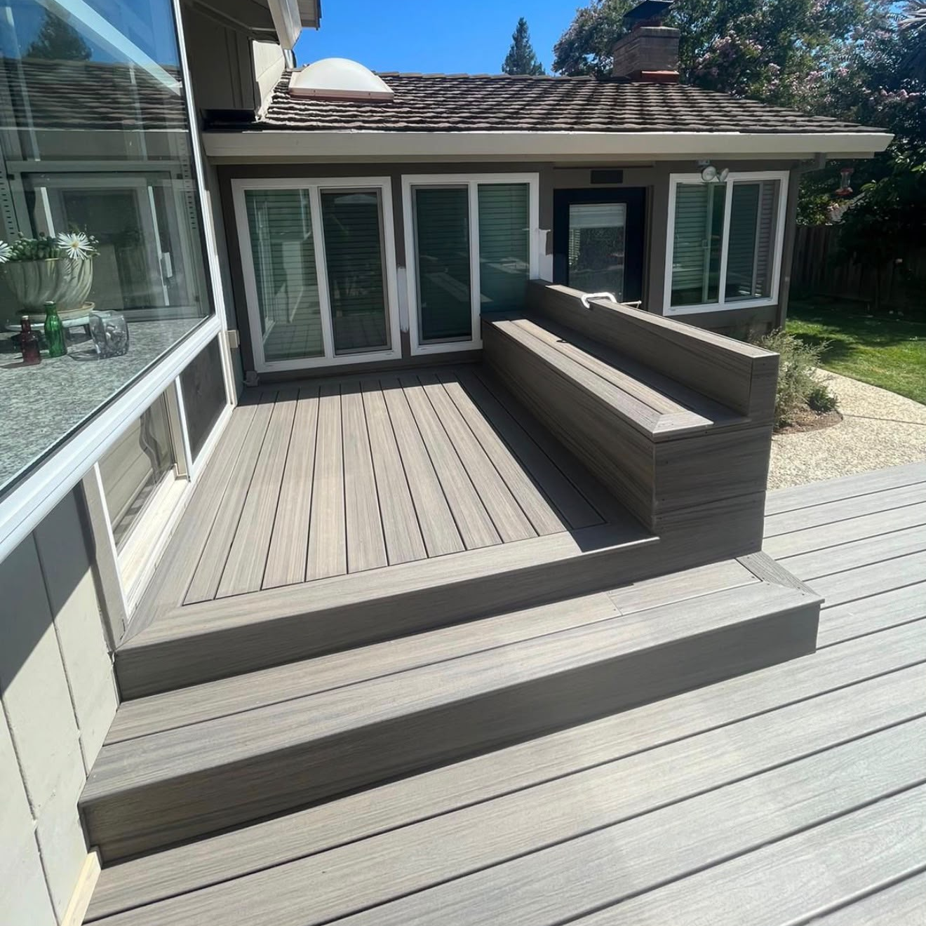Trex deck with a long built-in bench, framed landing, and broad steps beside the home's windows.